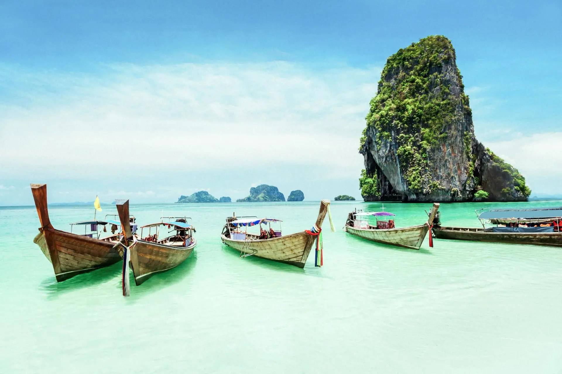 Traditional longtail boats in tropical turquoise waters with limestone cliffs
