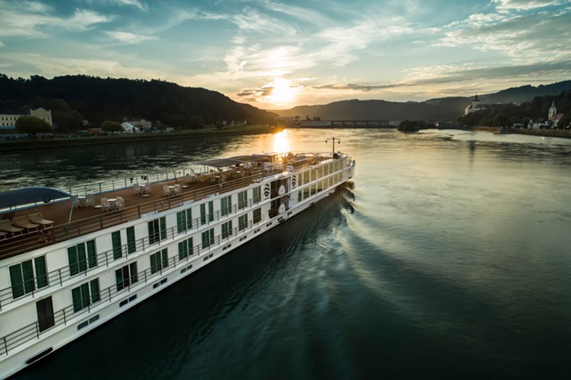 Uniworld river cruise ship at sunset navigating a scenic alpine river valley