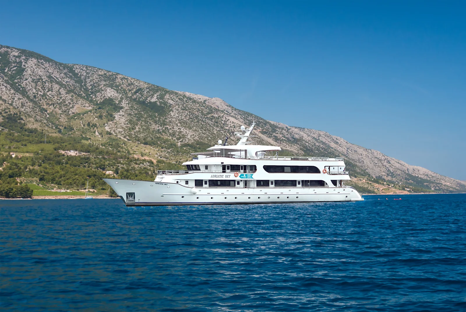 A sophisticated white luxury motor yacht named Adriatic Sky is anchored in crystal-clear blue