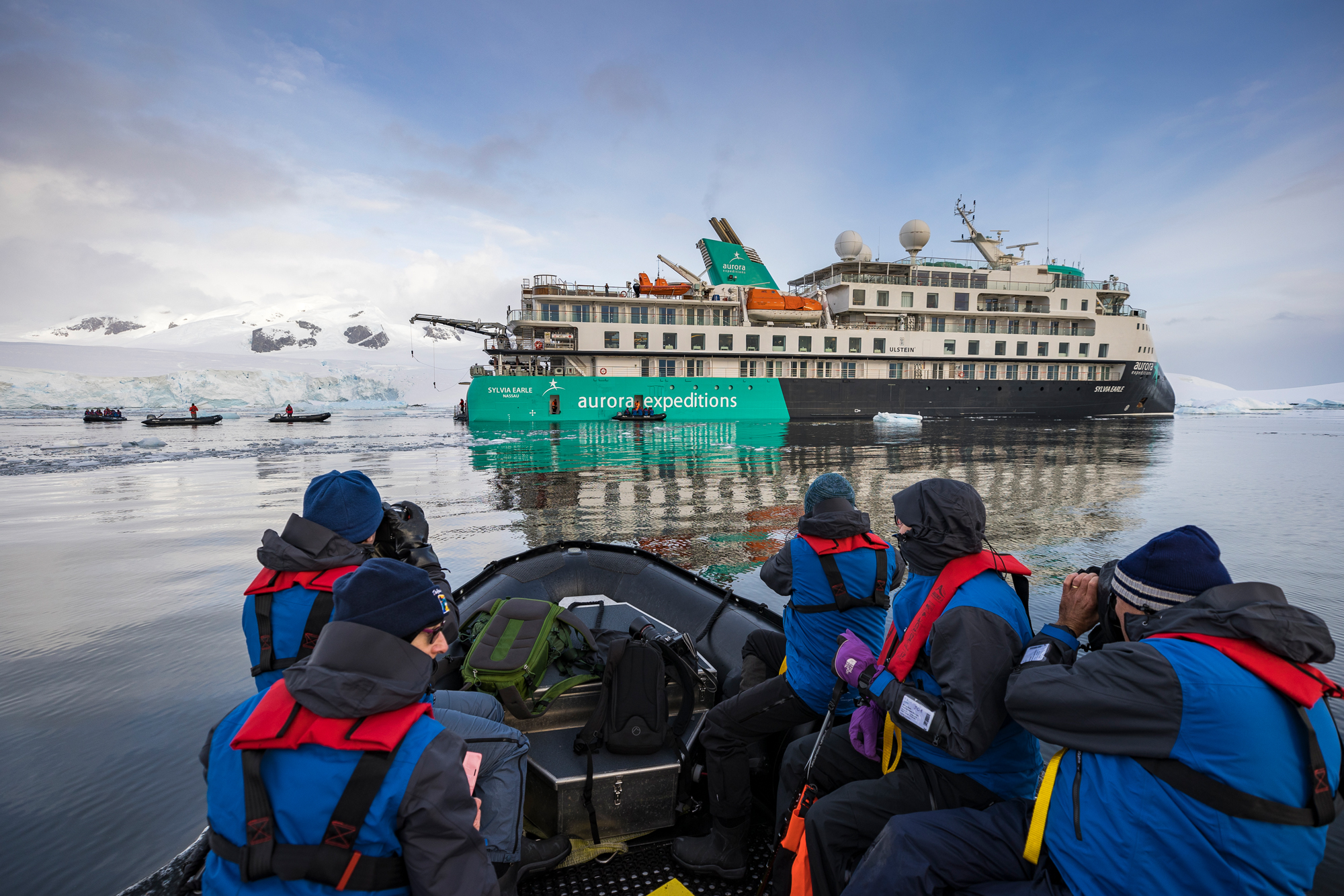 Antarctic Expedition Zodiac Cruise A group of travelers in blue and red waterproof gear ride a Zodiac boat near the Aurora Expeditions