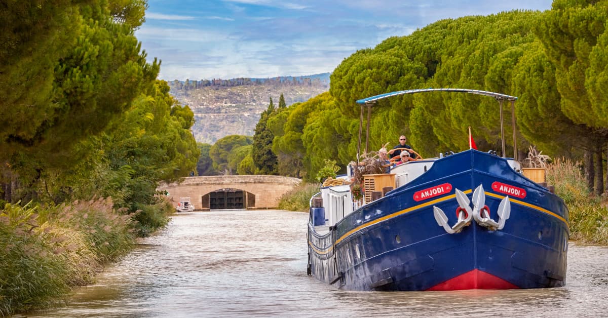 Barge Cruising Through European Canal Lock A traditional blue and gold barge named Anjobi navigates through a historic stone canal lock in