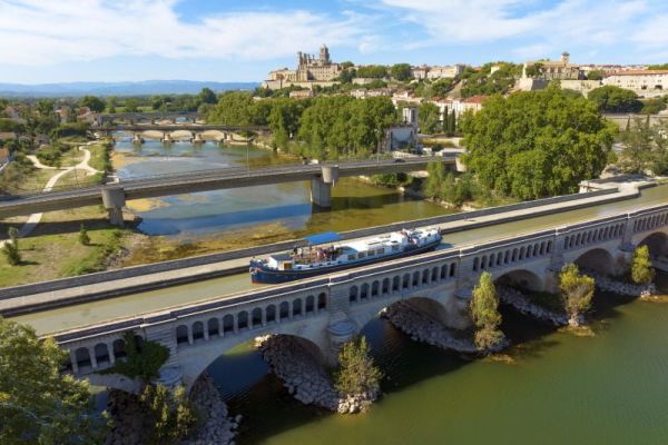 Barge Traversing Ancient French Waterway A modern river barge travels along the Lot River in southwestern France, passing beneath a historic