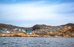 A picturesque coastal settlement nestled against arid, rocky hills viewed from the water
