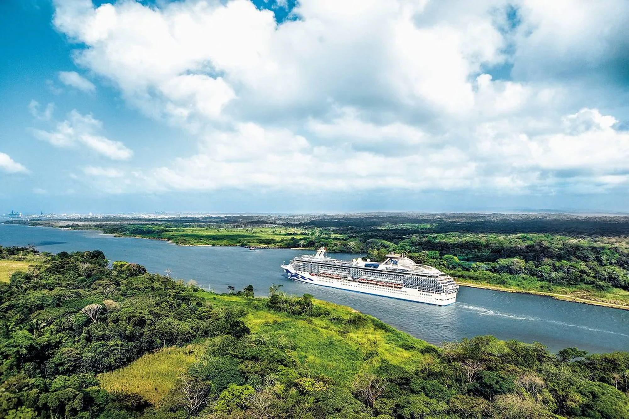 Cruise Ship Navigating Tropical Waterway A large white cruise ship sailing through a lush green landscape with dense forests and blue