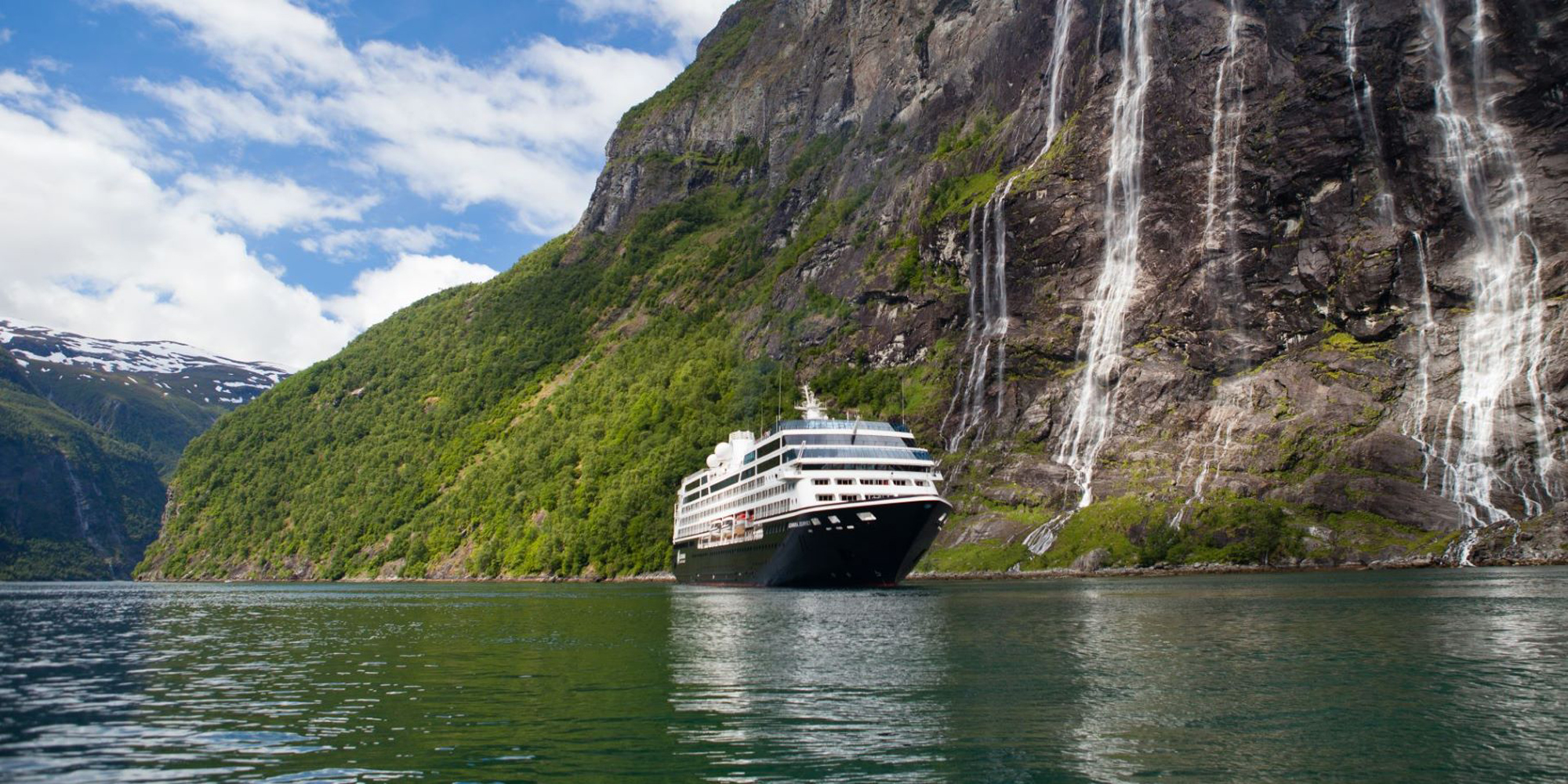Cruise Ship in Norwegian Fjord A white cruise ship sailing through a dramatic fjord landscape with steep, green-covered mountains and multiple waterfalls cascading down rocky cliffs.