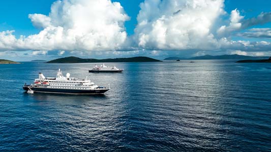 Cruise Ships on Calm Blue Waters Two white cruise ships anchored in a serene blue ocean with dramatic cloudy sky and mountainous