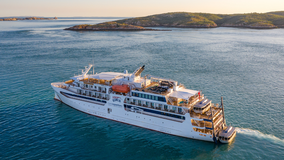 Expedition Cruise Ship in Coastal Waters Coral Expeditions ship navigating through blue coastal waters near rocky islands