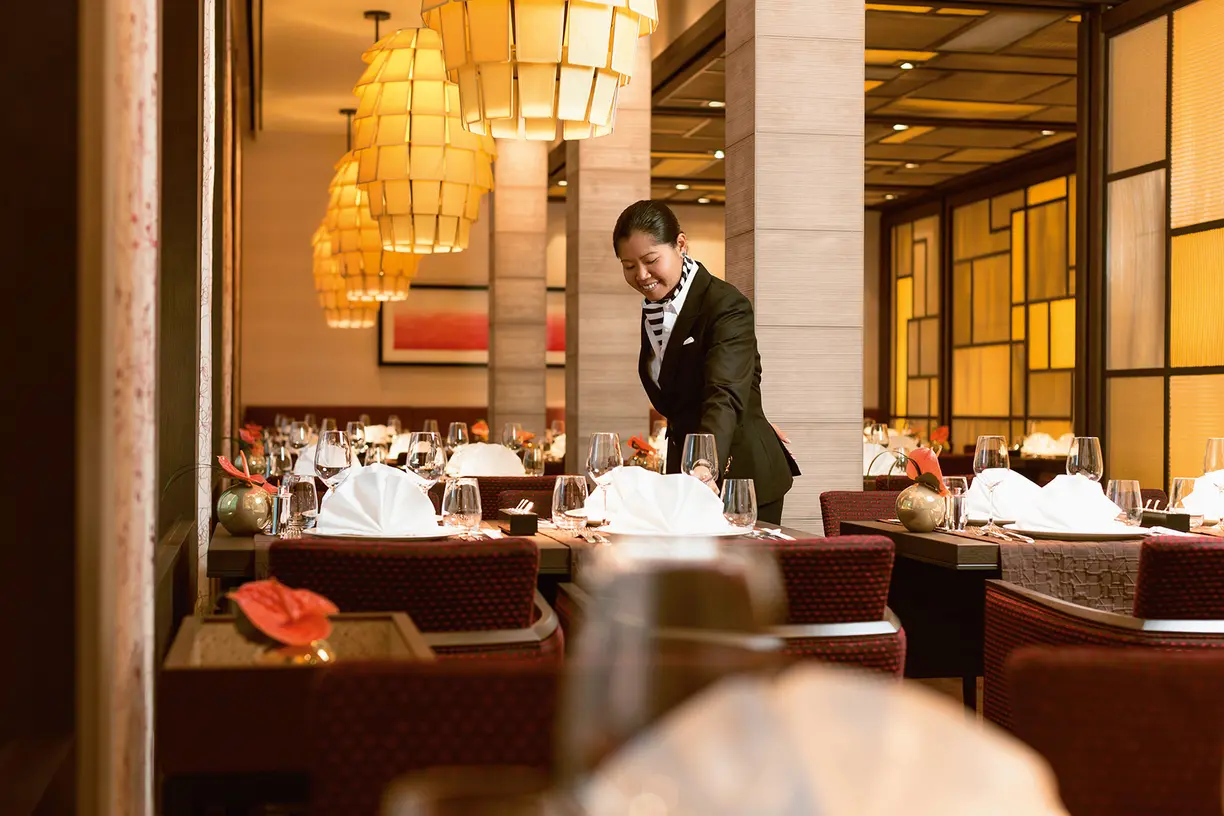 Elegant fine dining service aboard a Hapag-Lloyd luxury cruise ship with warm golden lighting and sophisticated place settings