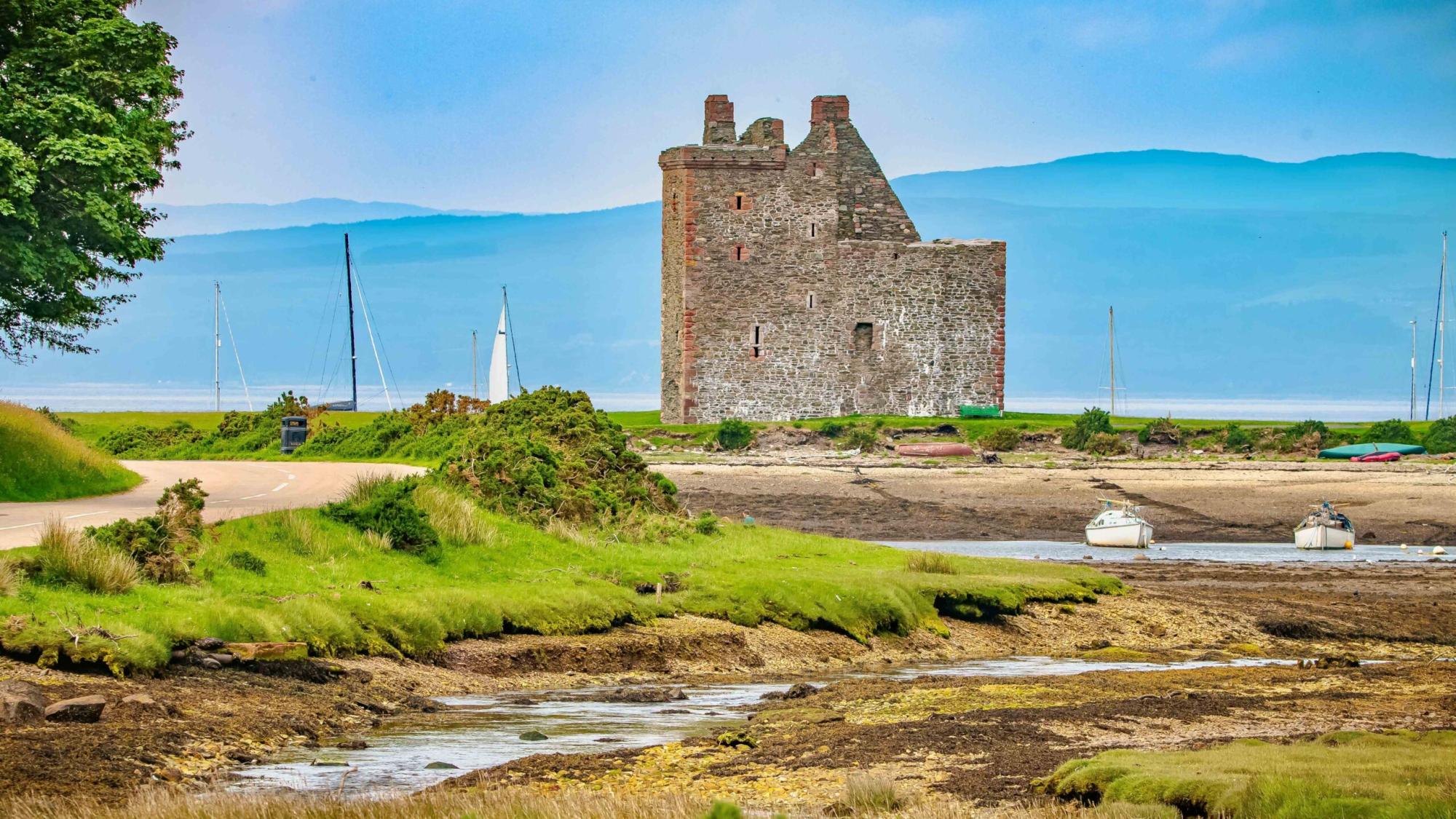 Historic Castle Ruins by Scottish Coastal Waters A picturesque medieval stone castle tower stands on the banks of a Scottish estuary, surrounded
