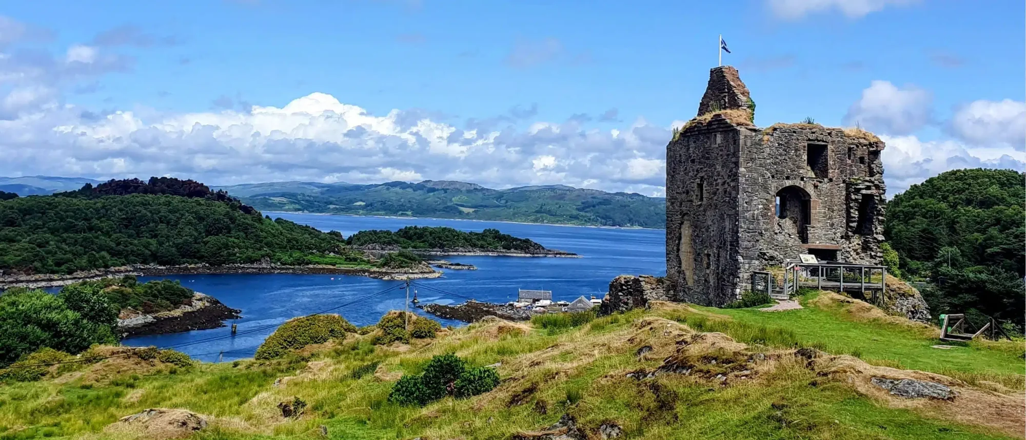 Historic Castle Ruins on Scottish Coastline A dramatic stone castle ruin with a flagpole stands on a green clifftop overlooking a picturesque