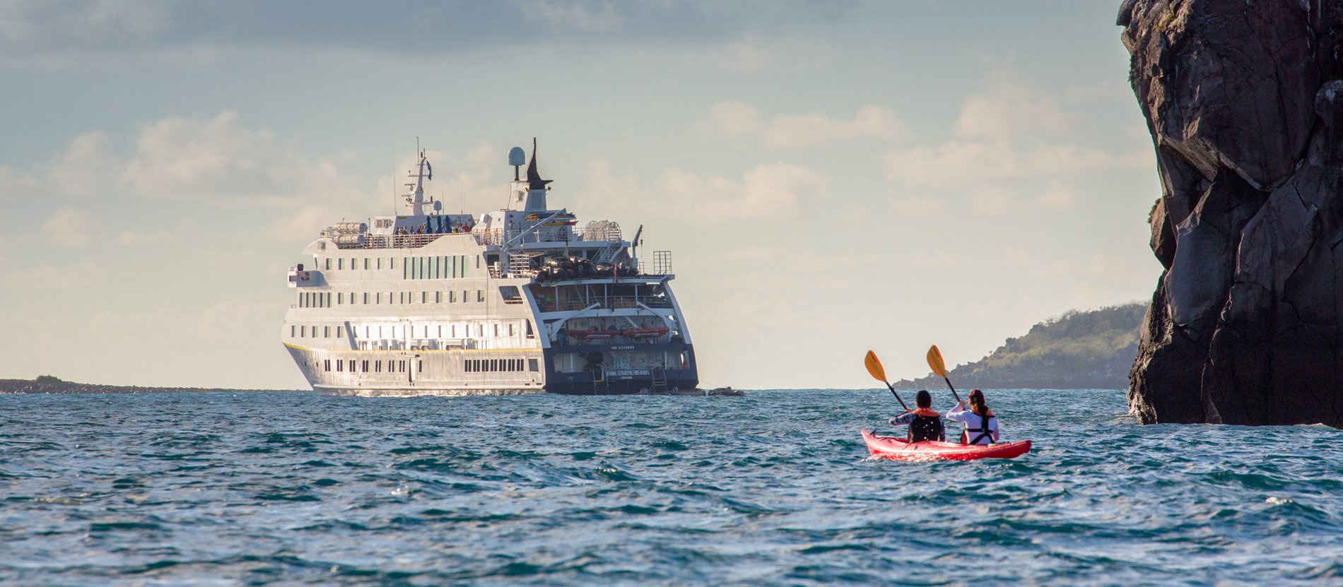 Kayaking Adventure Near Cruise Ship Two kayakers in a red kayak paddle near dramatic limestone cliffs while a large white cruise ship