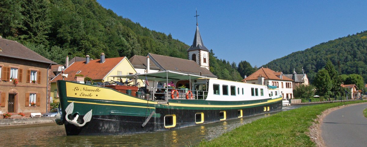 La Nouvelle Étoile Barge in European Canal Village A traditional green and yellow canal barge named 'La Nouvelle Étoile' navigates through