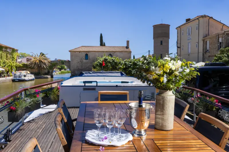 Luxury Barge Dining Deck on European Canal An elegant outdoor dining setup on the deck of a luxury river barge moored along a scenic European