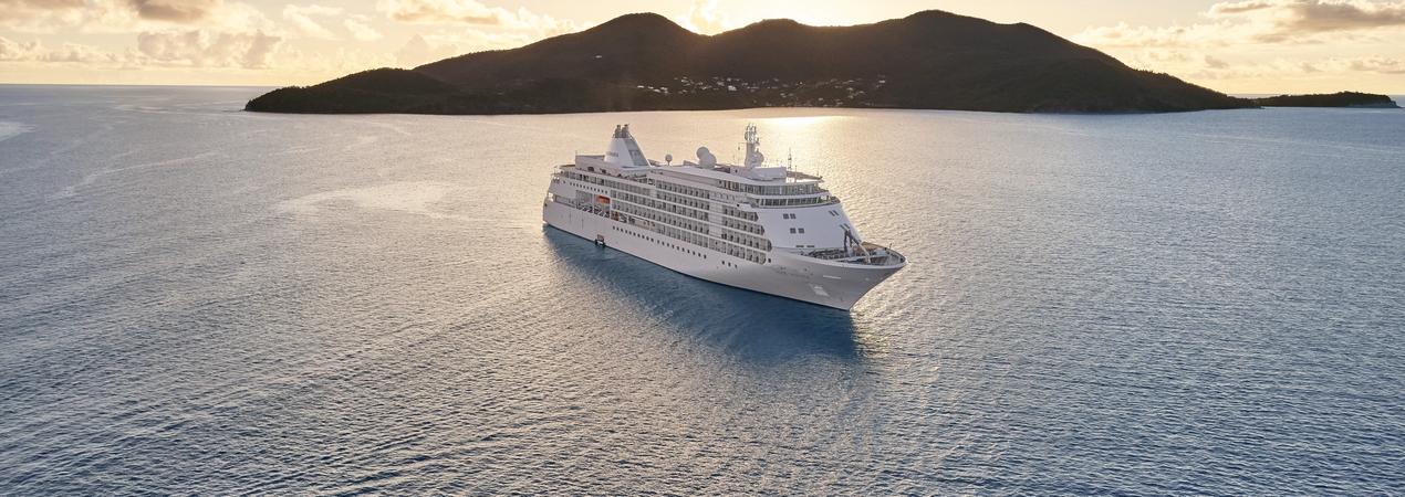 Luxury Cruise Ship Near Tropical Island A white luxury cruise ship anchored near a mountainous island during golden hour, with calm waters