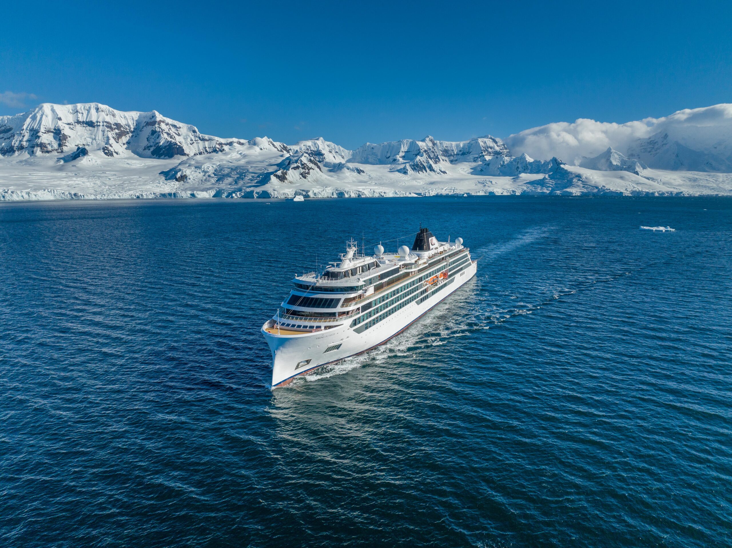 Luxury Cruise Ship in Antarctic Waters A white cruise ship sailing through deep blue waters with a dramatic snow-covered mountain