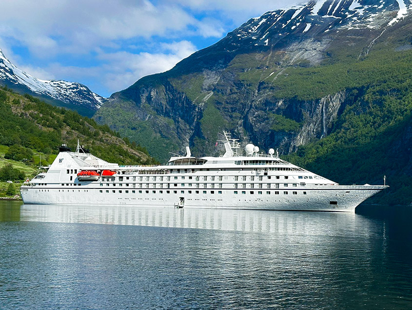Luxury Cruise Ship in Norwegian Fjord A pristine white cruise ship anchored in a serene Norwegian fjord, surrounded by dramatic