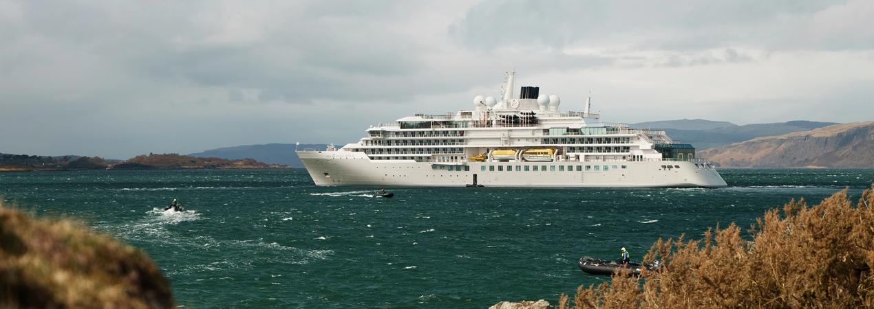 Luxury Cruise Ship in Rugged Coastal Landscape A white luxury cruise ship anchored in a turquoise ocean with rocky coastline and mountains in