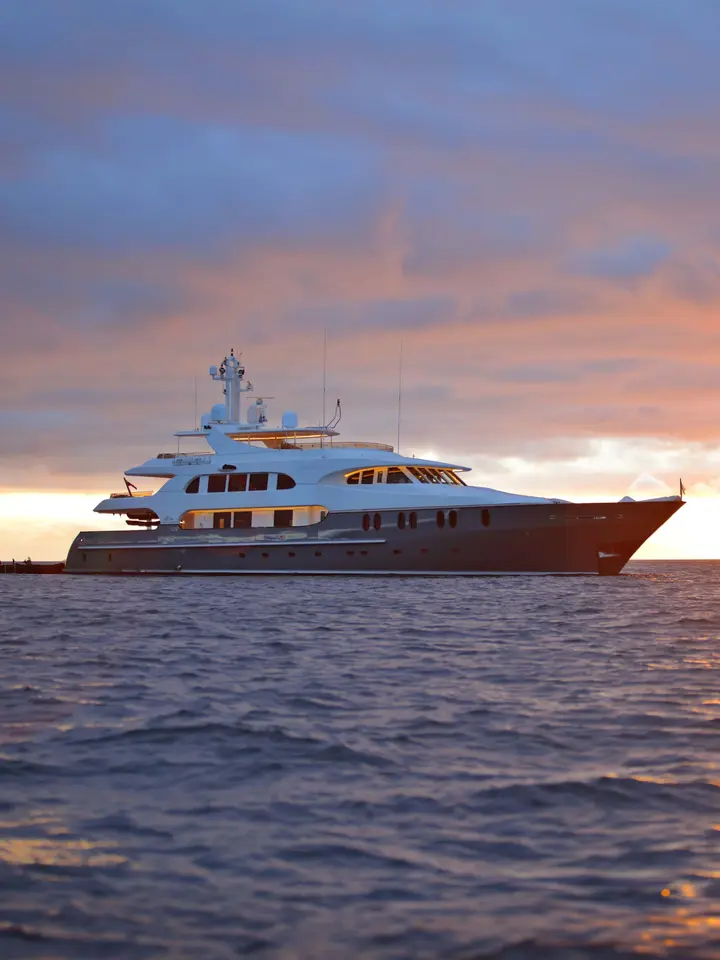 A stunning multi-deck luxury yacht is anchored in calm waters during golden hour, with warm