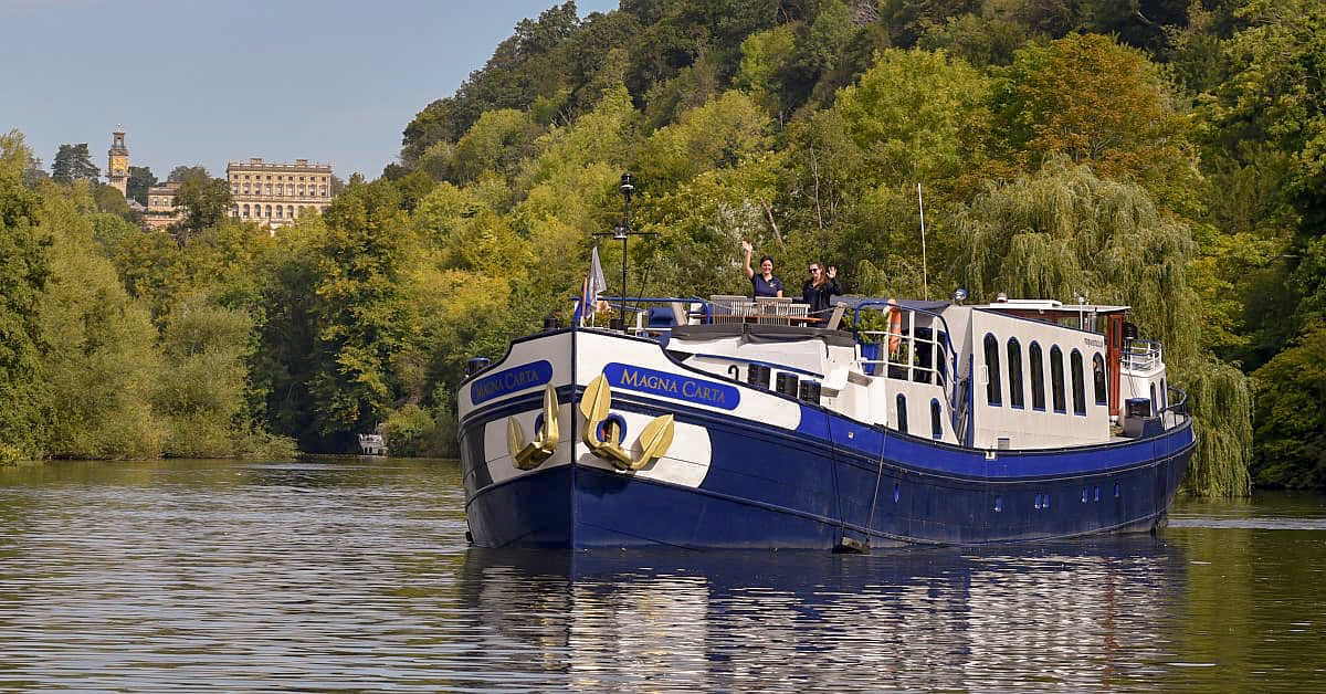 Magna Carta River Barge on European Waterway A luxury river cruise barge named Magna Carta navigates a picturesque European river surrounded