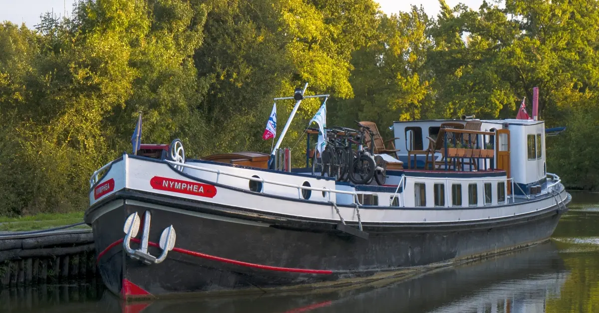 Nymphea Barge Moored Along European Waterway A charming traditional European barge named Nymphea is moored along a peaceful riverside, featuring
