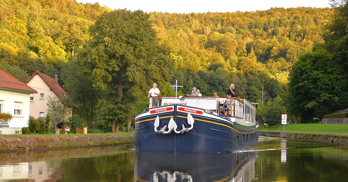 River Barge on Scenic European Waterway A traditional blue river barge named 'Panache' navigates a calm European canal with passengers