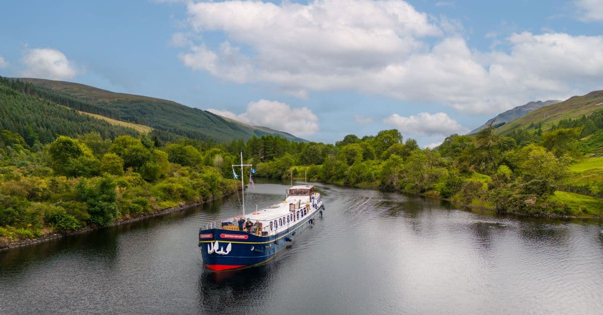 River Cruise Boat in Scottish Highlands A picturesque river cruise vessel navigates through calm waters surrounded by lush green mountains