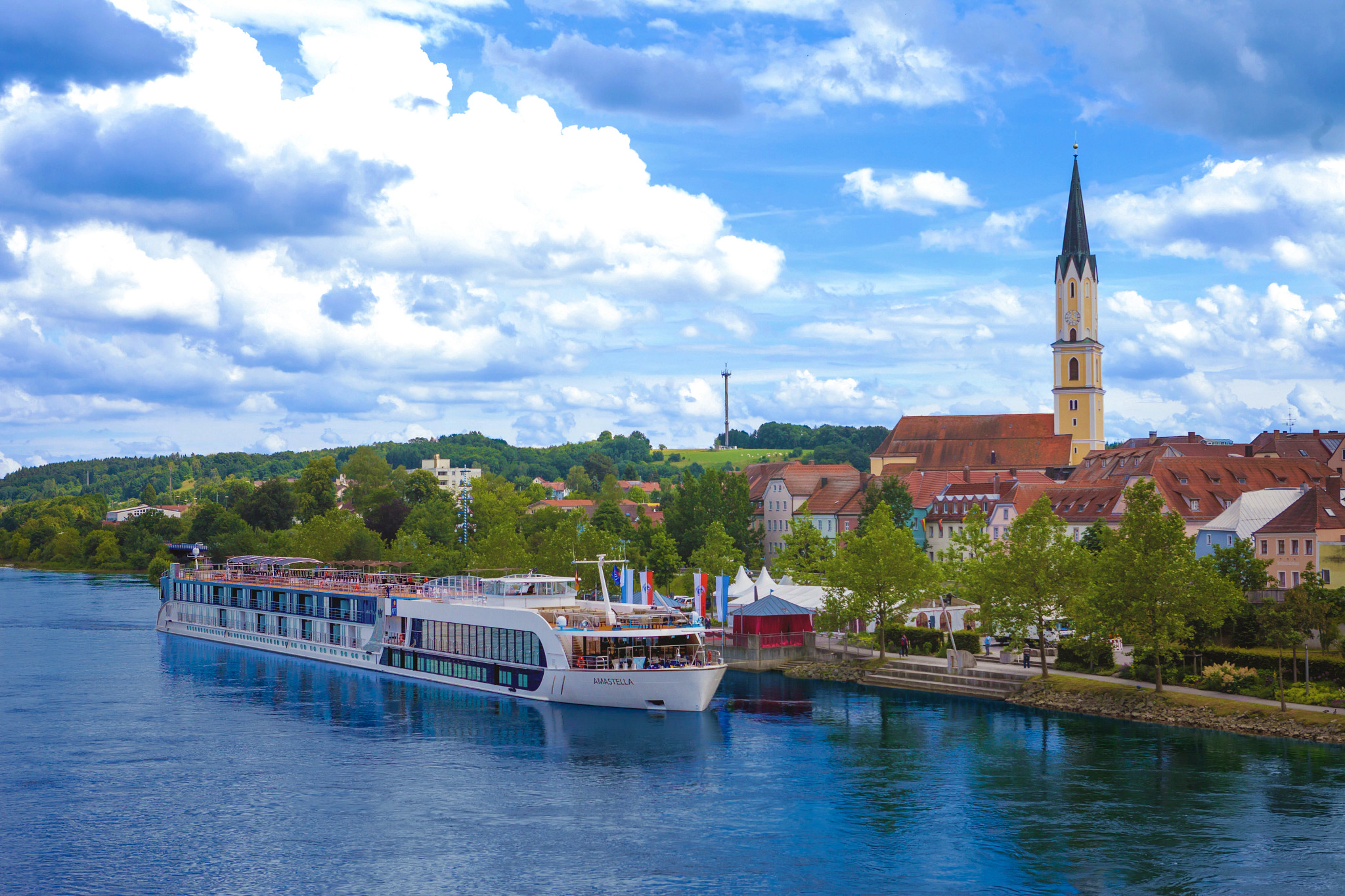 River Cruise Ship in European Riverside Town A modern river cruise ship docked alongside a picturesque European town with a tall church spire