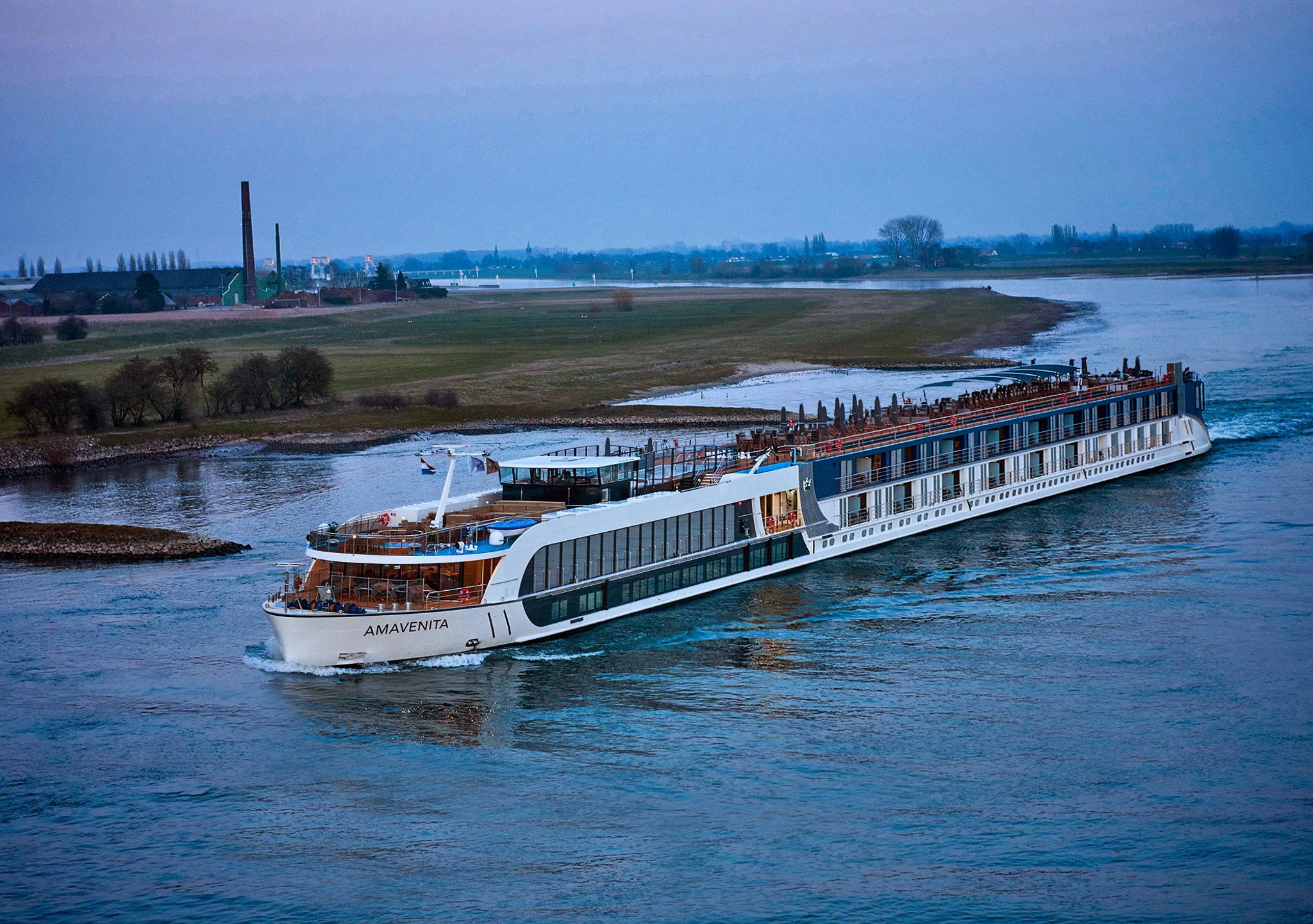 River Cruise Ship on Scenic Waterway A modern river cruise ship named Amavenita sailing along a tranquil river with grassy banks