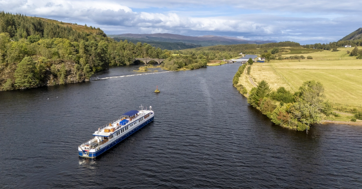 River Cruise Vessel on Scottish Waterway A scenic river cruise ship navigates through a picturesque Scottish valley, surrounded by lush
