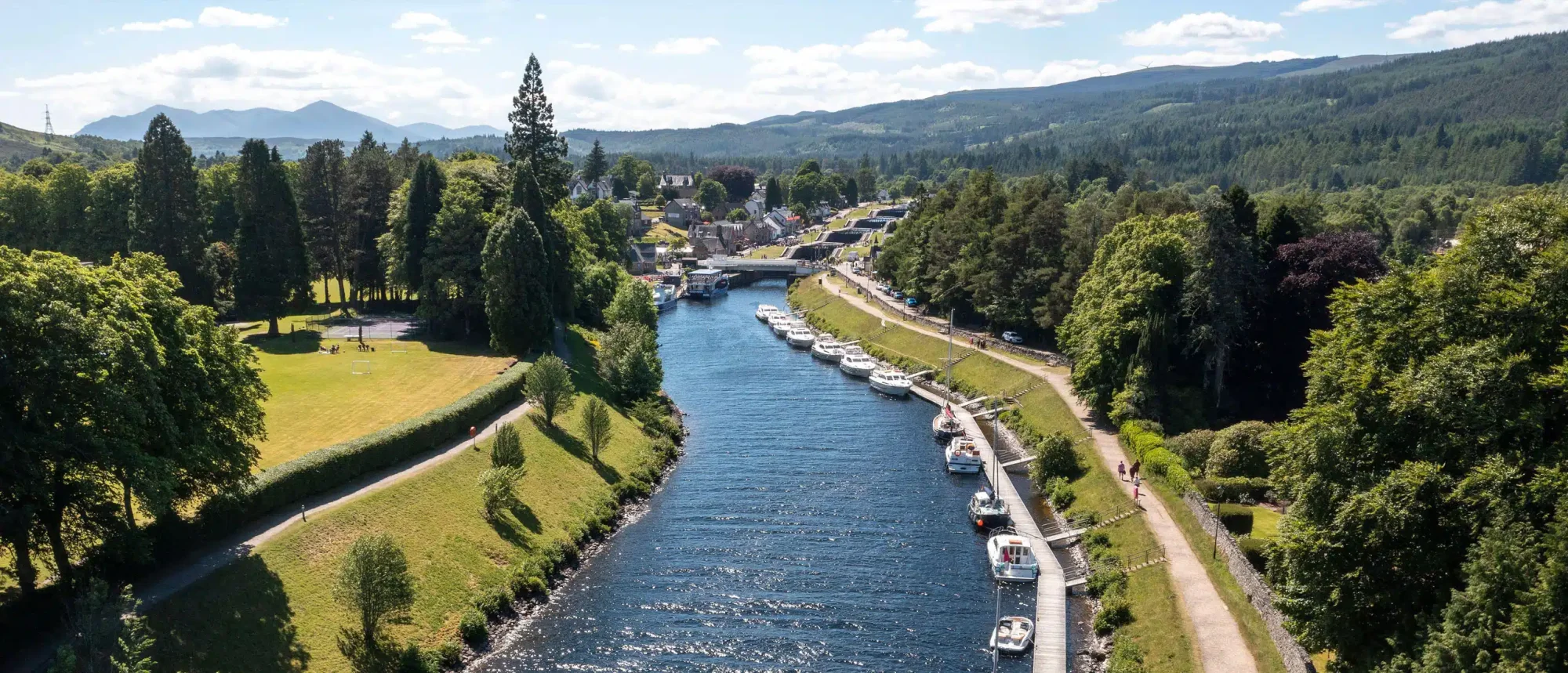 River Town with Moored Boats and Mountain Views An idyllic riverside town nestled in a forested valley with numerous pleasure boats and small