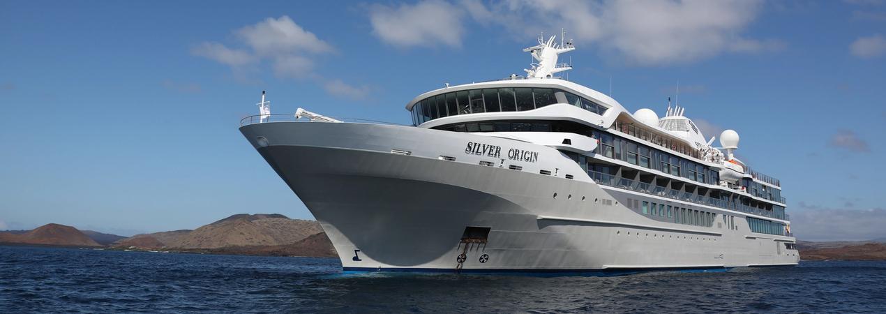 Silver Origin Cruise Ship at Sea A sleek, white luxury cruise ship named Silver Origin sailing on blue waters with rocky islands