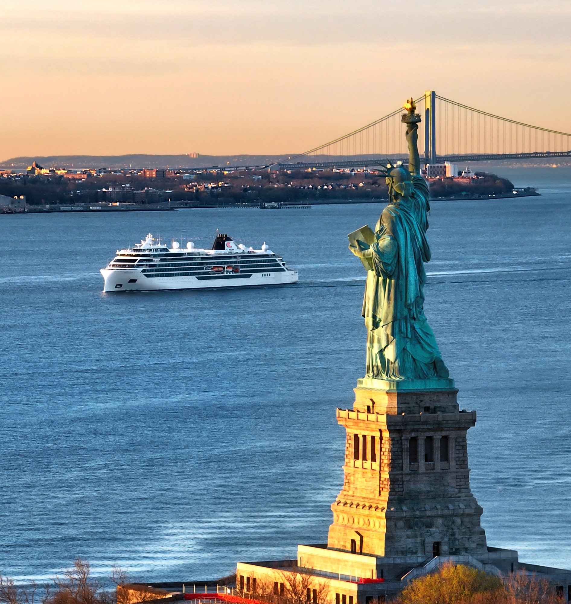 Statue of Liberty and Cruise Ship in New York Harbor A luxurious white cruise ship sails past the Statue of Liberty at sunset, with
