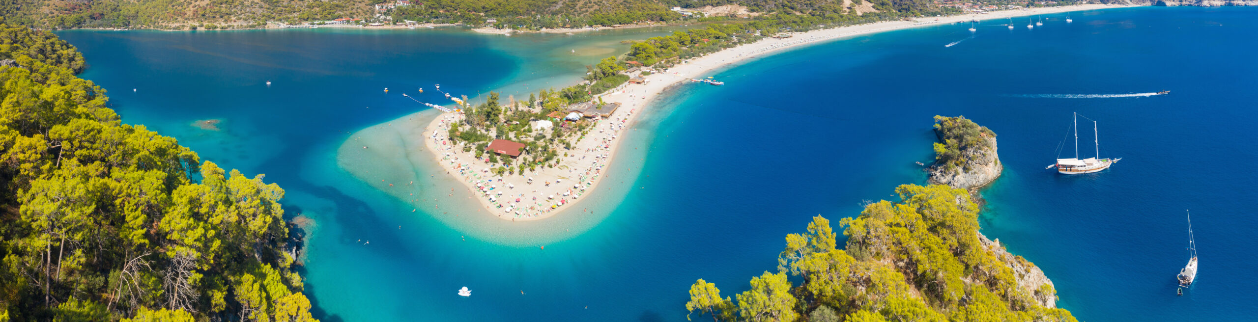 An aerial view of a unique sandy peninsula with white beaches extending into turquoise blue waters