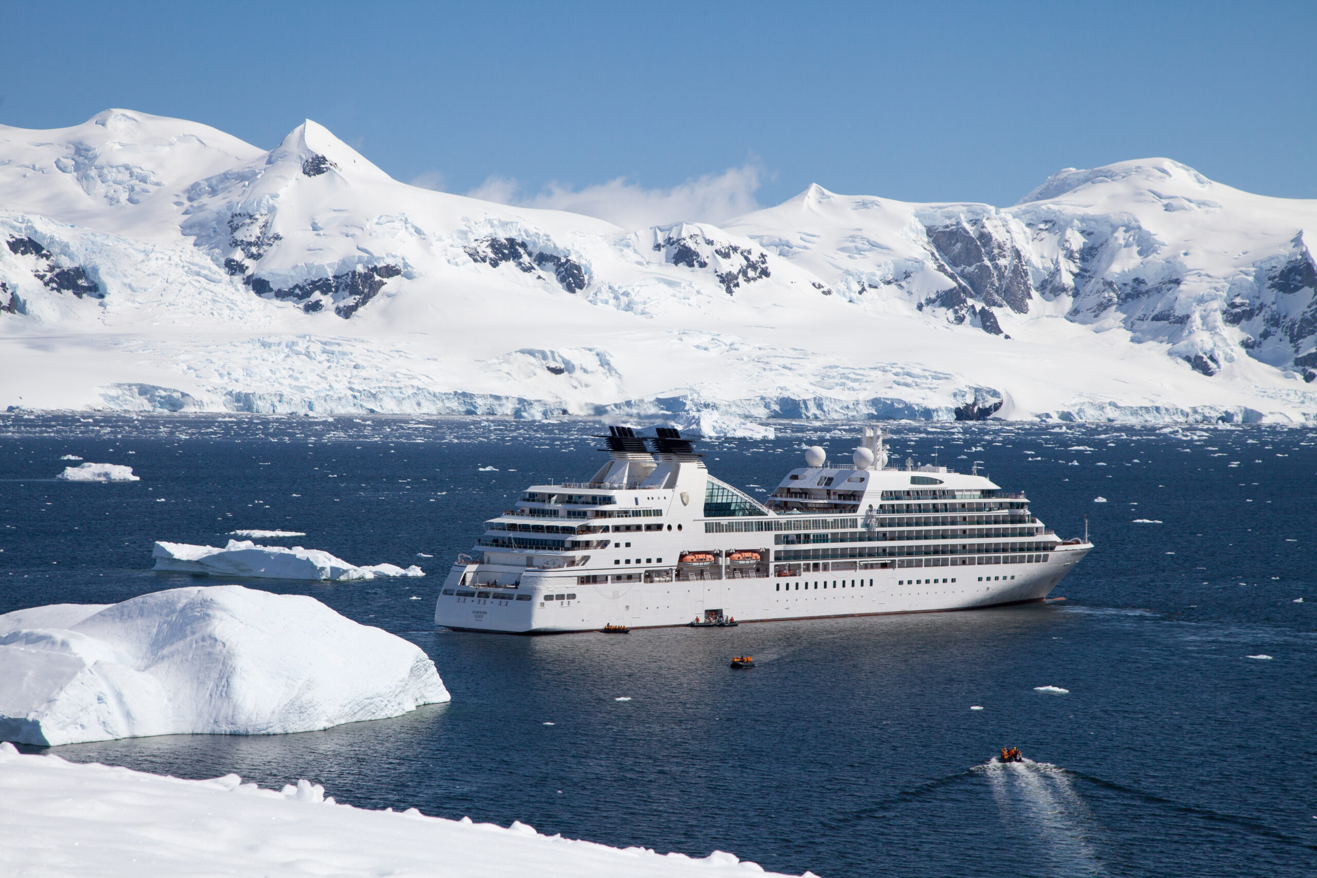 YR15_neko-point-8377 Luxury cruise ship anchored in Antarctic waters with snow-covered mountains and icebergs visible