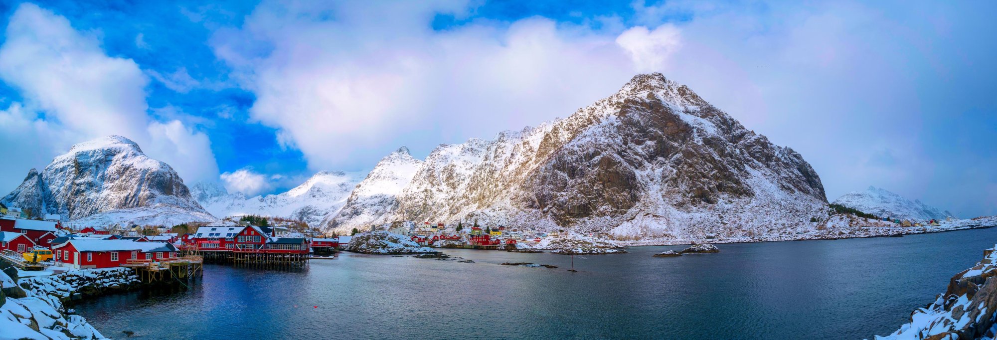 shutterstock_1922095100 Dramatic Norwegian fjord scenery with towering cliff faces, cascading waterfalls, and mirror-still waters reflecting snow-capped mountains under a bright northern sky.