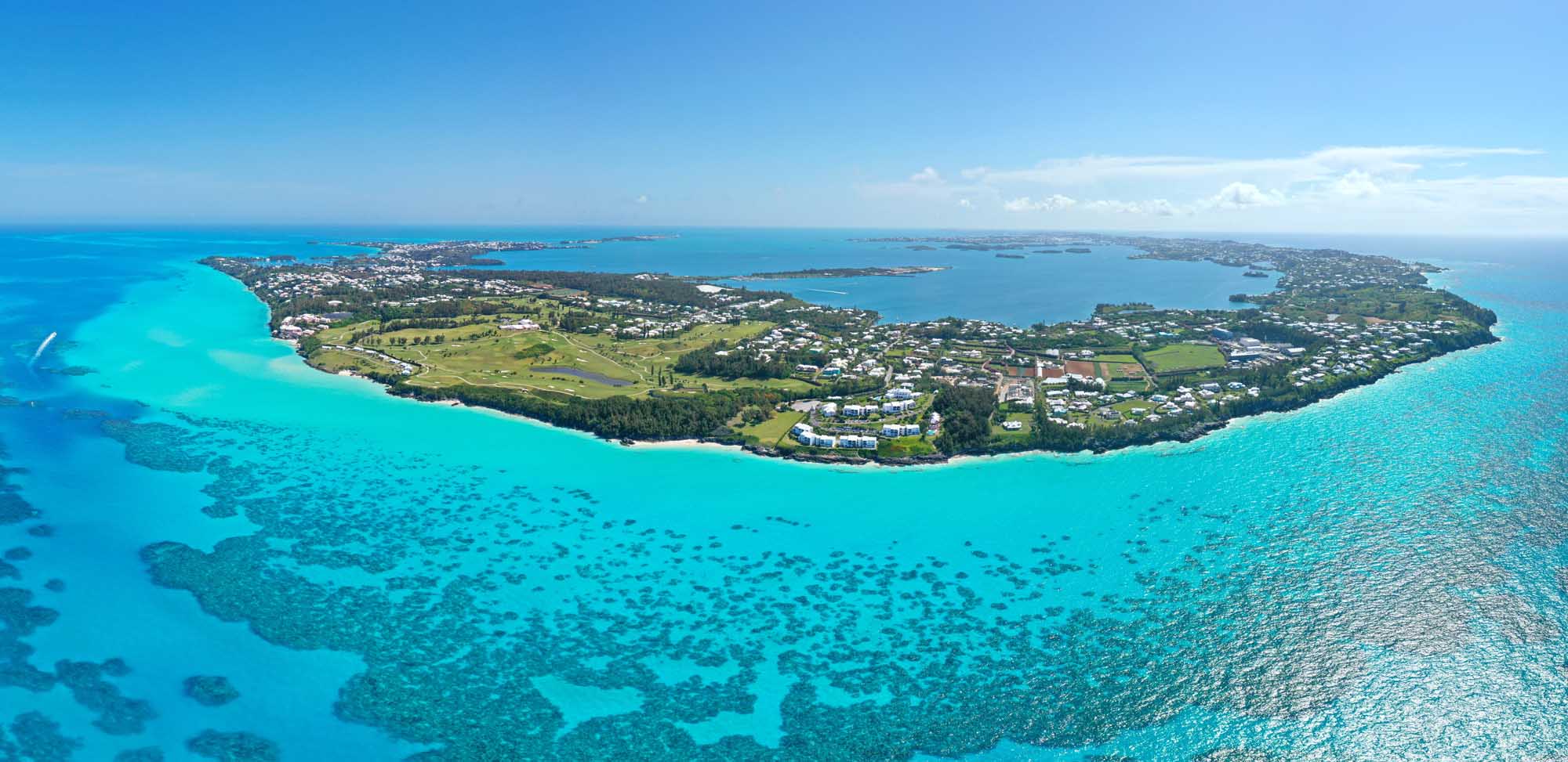 An aerial photograph of Bermuda island surrounded by stunning turquoise Atlantic Ocean waters, showcasing the island's lush green vegetation, residential areas, and pristine beaches.