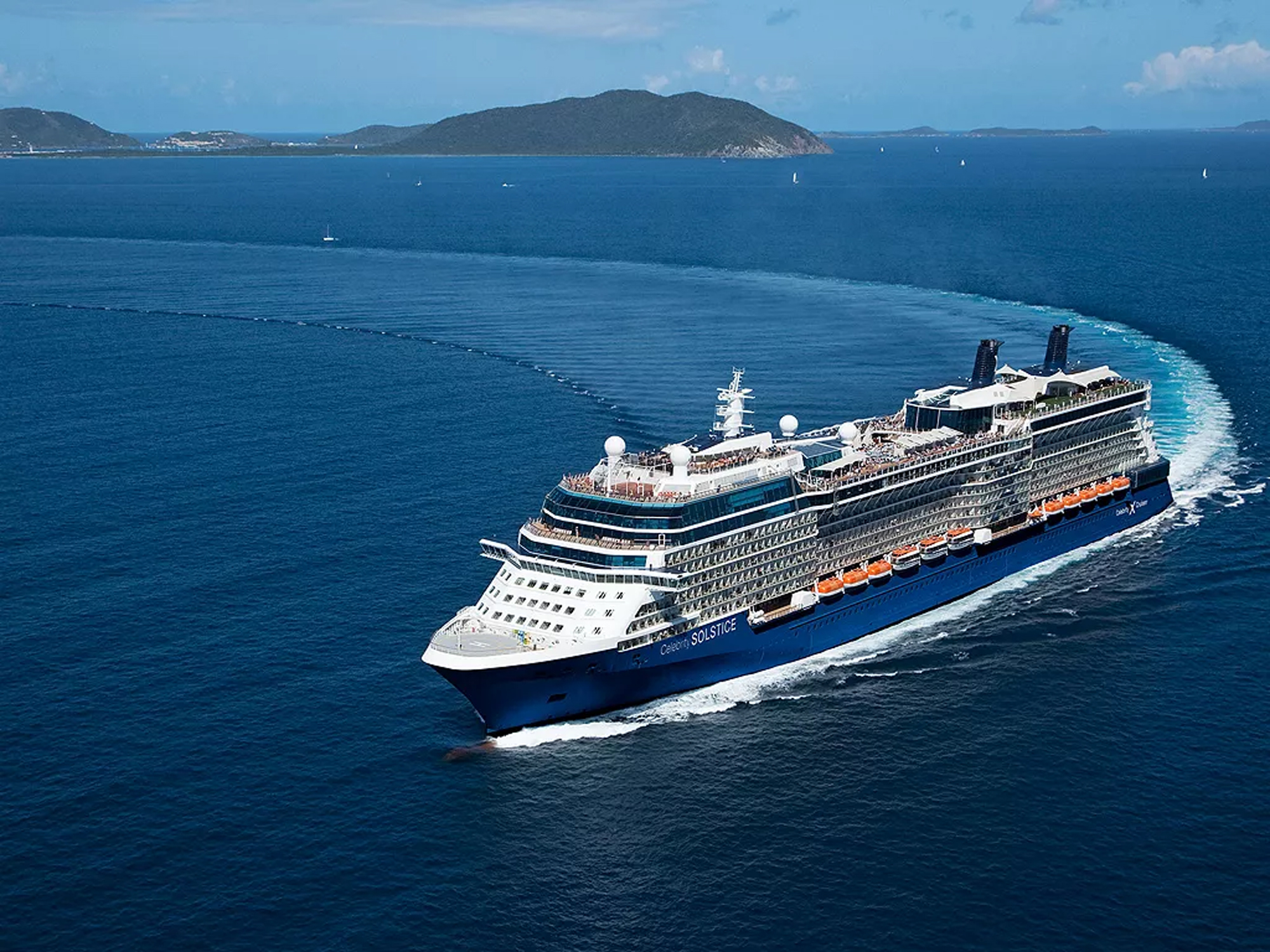 Celebrity Solstice Cruise Ship at Sea Celebrity Solstice cruising through crystal-clear tropical waters near a mountainous island coastline
