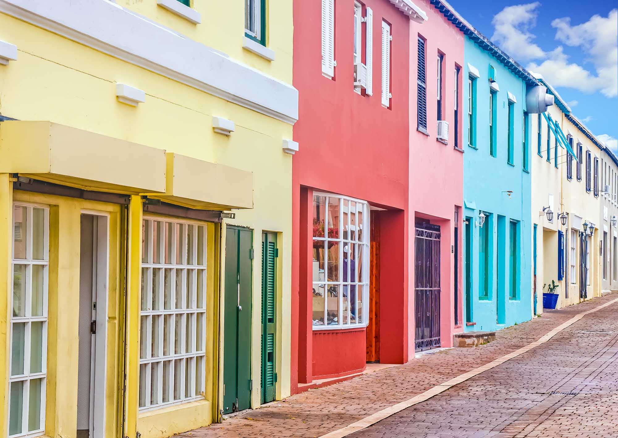A picturesque street lined with vibrant pastel-colored colonial buildings featuring yellow, pink, turquoise, and cream facades.