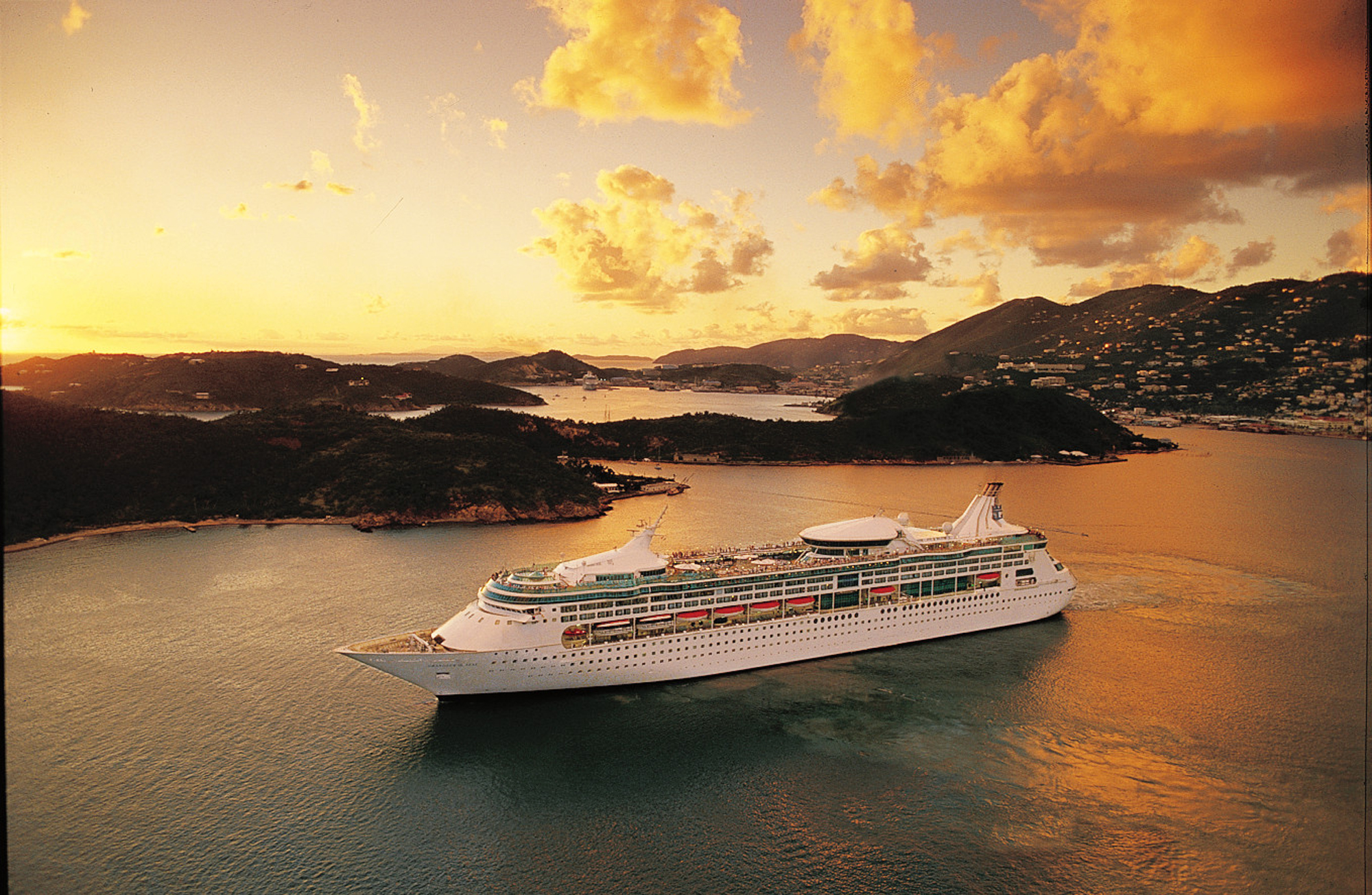 A large Royal Caribbean Vision-class cruise ship anchors in calm turquoise waters surrounded