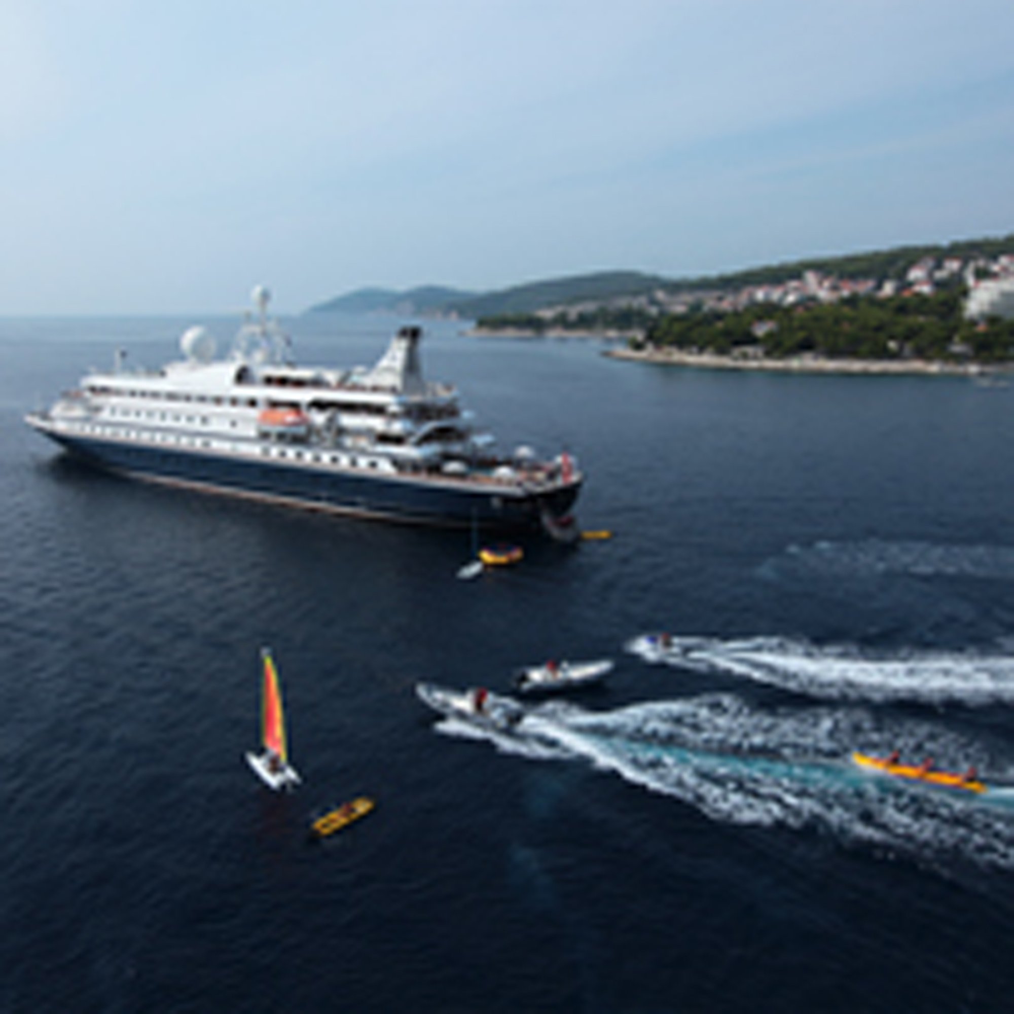 Cruise Ship with Water Sports Activities A large cruise ship anchored in calm Mediterranean waters with jet skis and water sports equipment