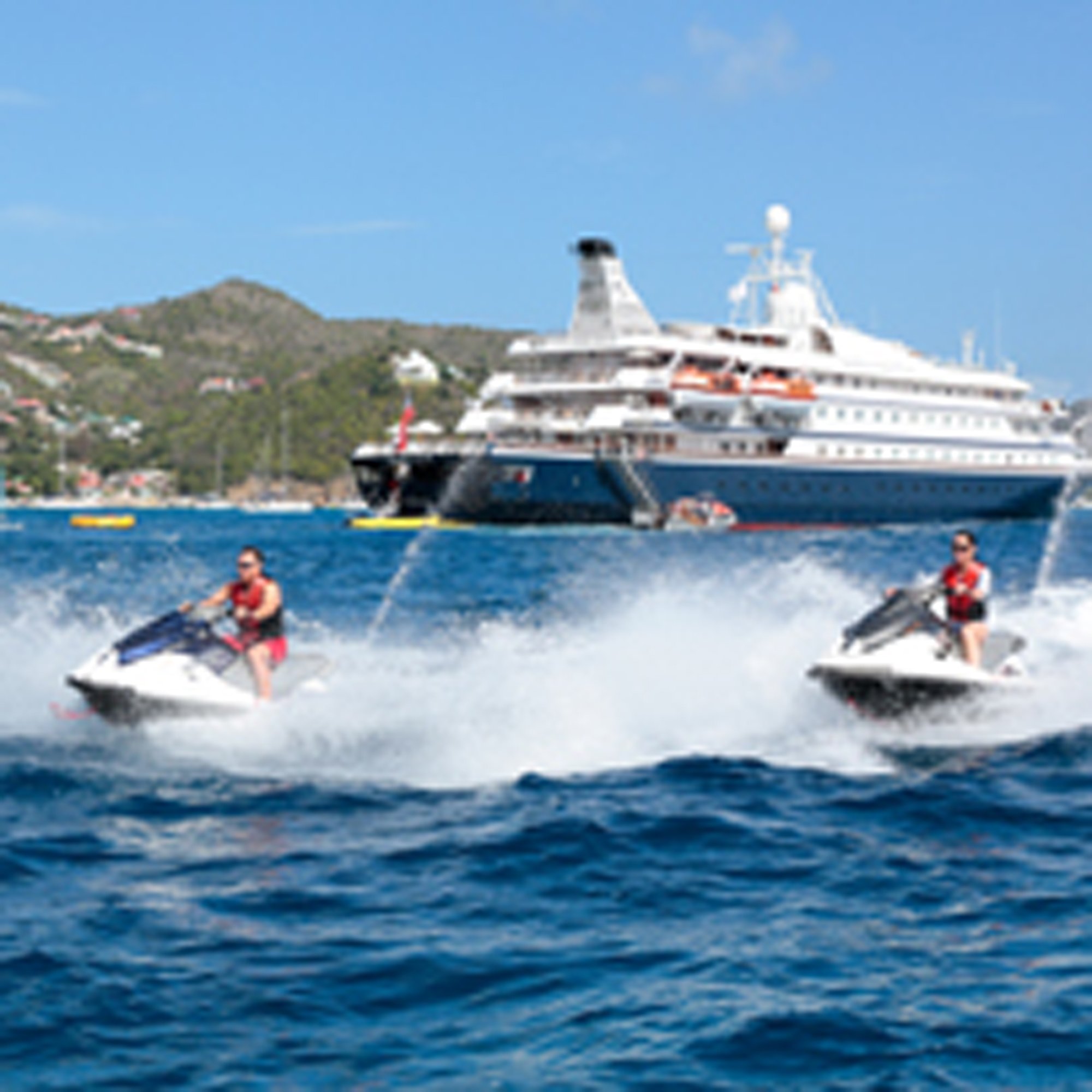 Jet Ski Adventure Near Cruise Ship Two jet skiers in red life vests enjoy water sports in front of a large cruise ship anchored in