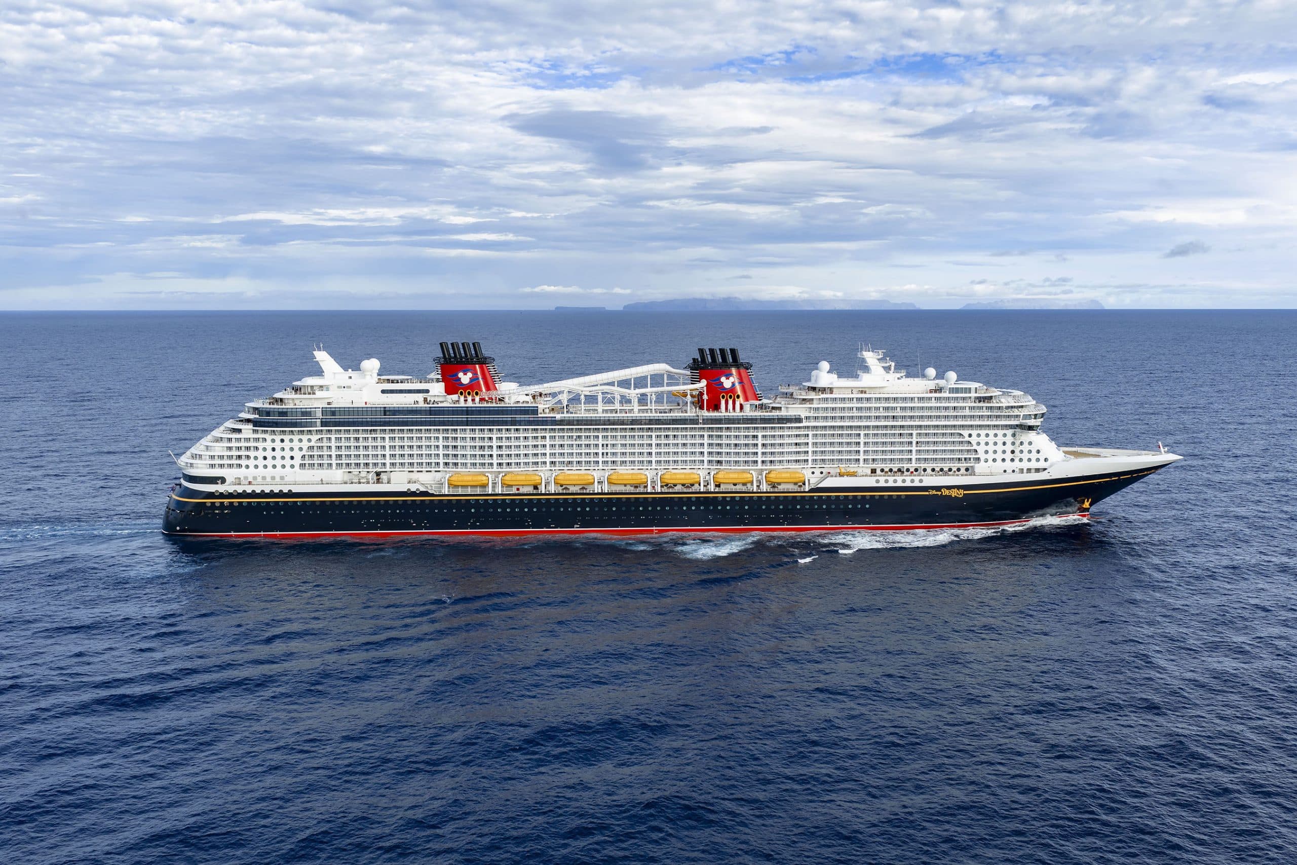 Large Cruise Ship at Sea with Mountains A massive modern cruise ship with white superstructure and black hull featuring distinctive red