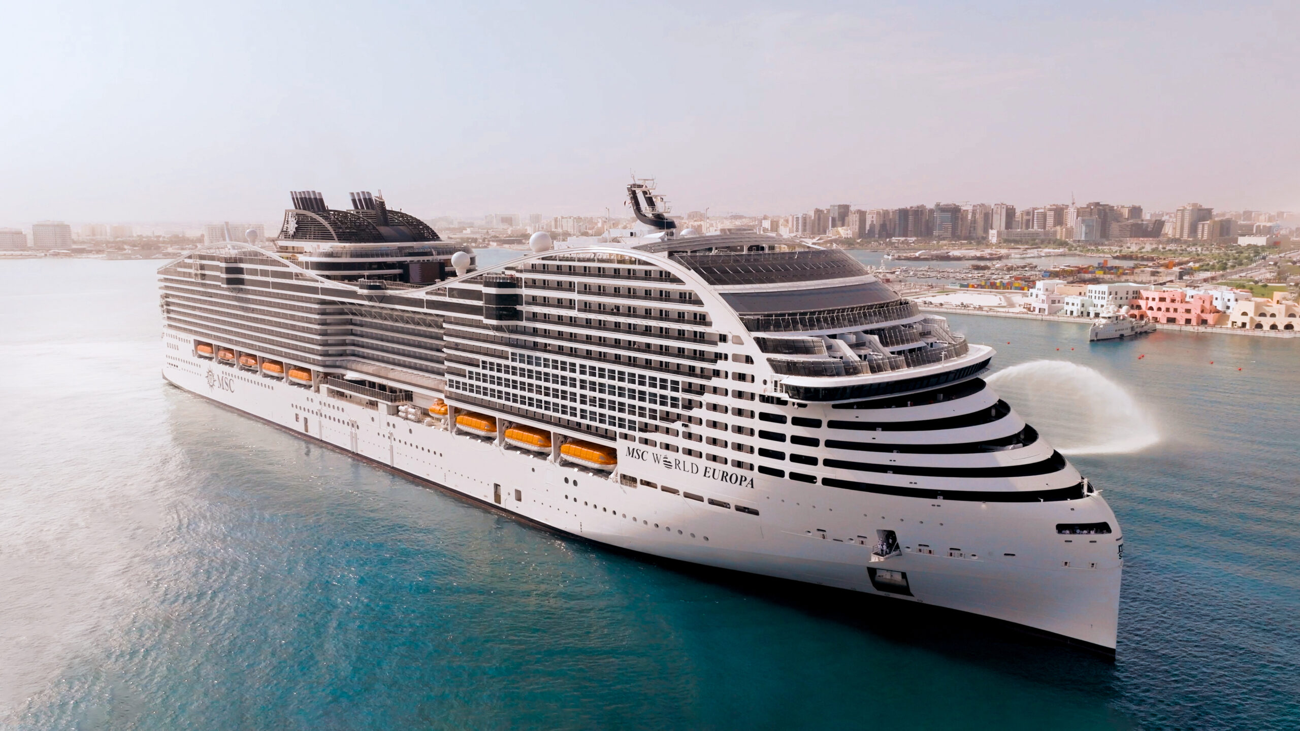 MSC World Europa cruise ship anchored in a Mediterranean port with colorful waterfront town