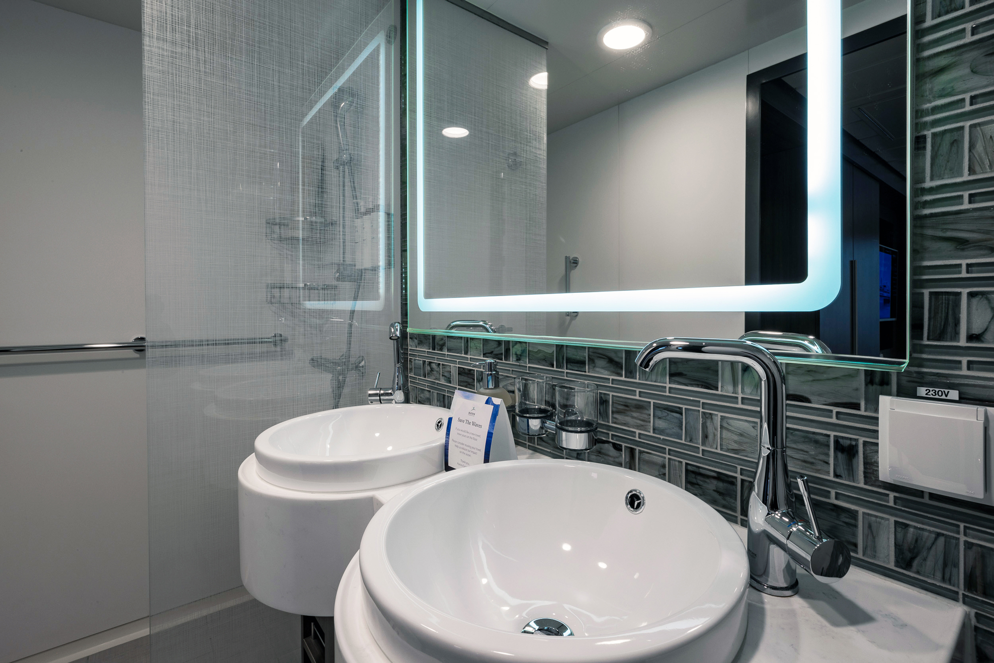 Modern Cruise Ship Bathroom with LED Mirror A contemporary bathroom aboard a cruise ship featuring dual white circular vessel sinks, a sleek