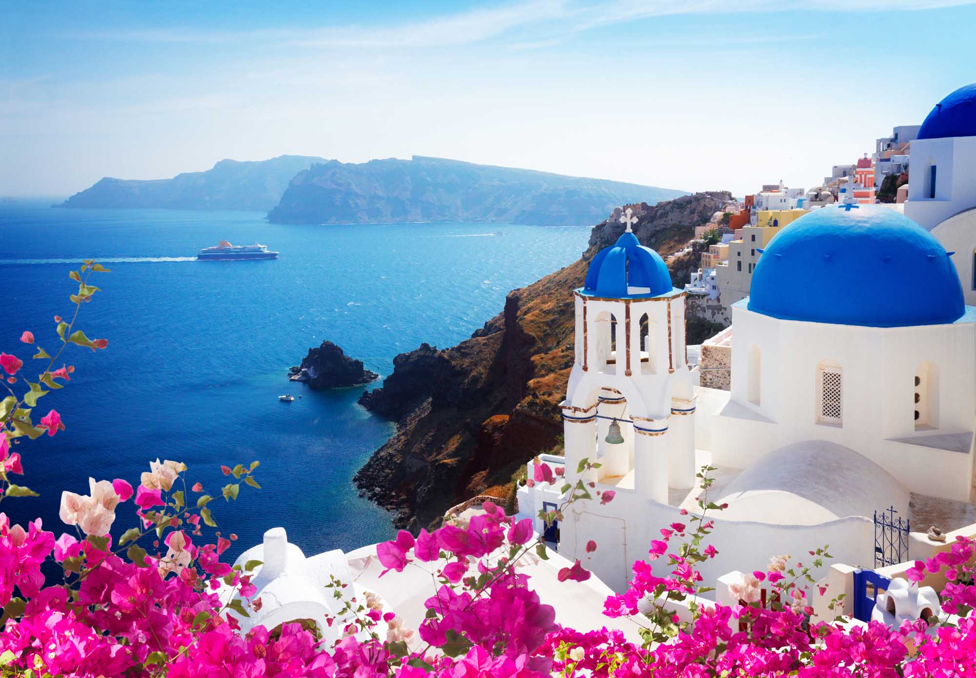 Santorini Cliffside Village with Blue-Domed Church A picturesque view of Oia village in Santorini, Greece, featuring iconic white-washed buildings with brilliant blue-domed churches overlooking the deep blue Aegean Sea.