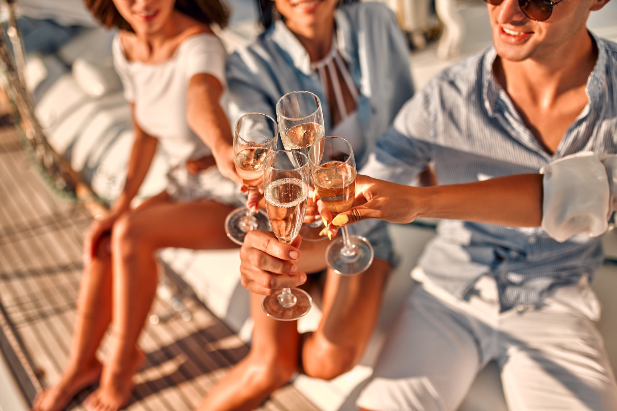 adobestock-380276171 A group of elegantly dressed passengers aboard a cruise ship clink champagne glasses together in a celebratory toast during golden hour.