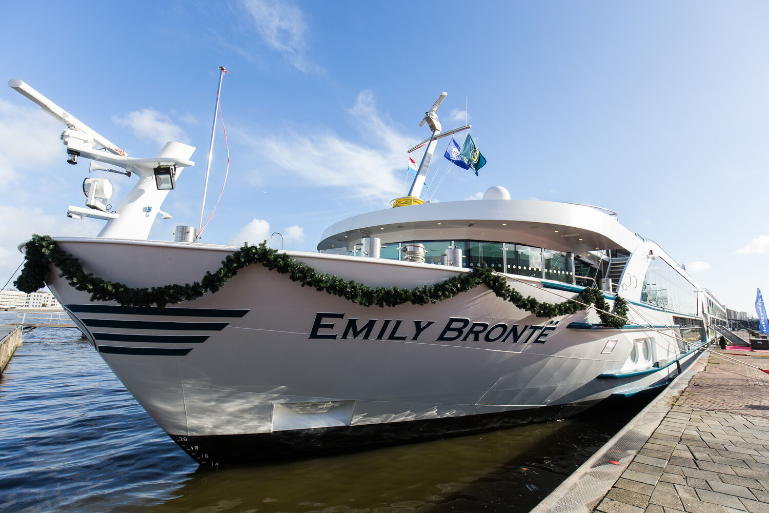 The MS Emily Brontë, a Riviera River Cruises vessel, is moored at a riverside dock adorned