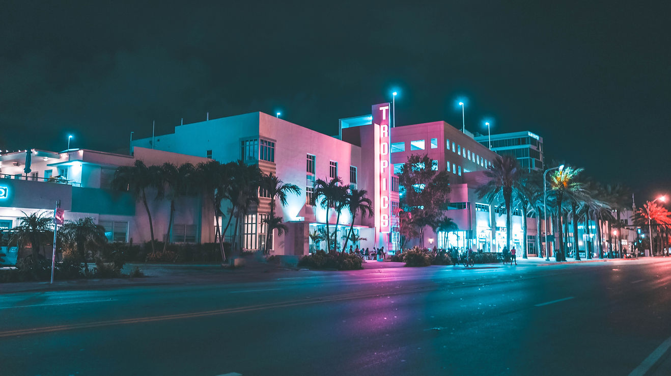 A vibrant nighttime cityscape featuring striking Art Deco buildings illuminated by vivid cyan