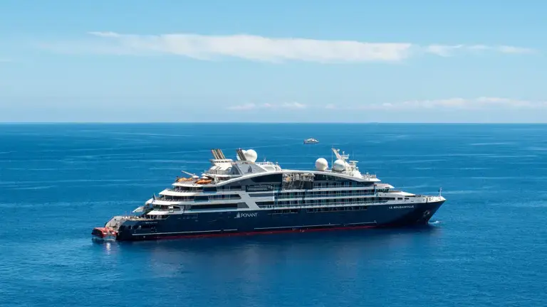 Ponant cruise ship sailing in turquoise waters with sea lions swimming nearby